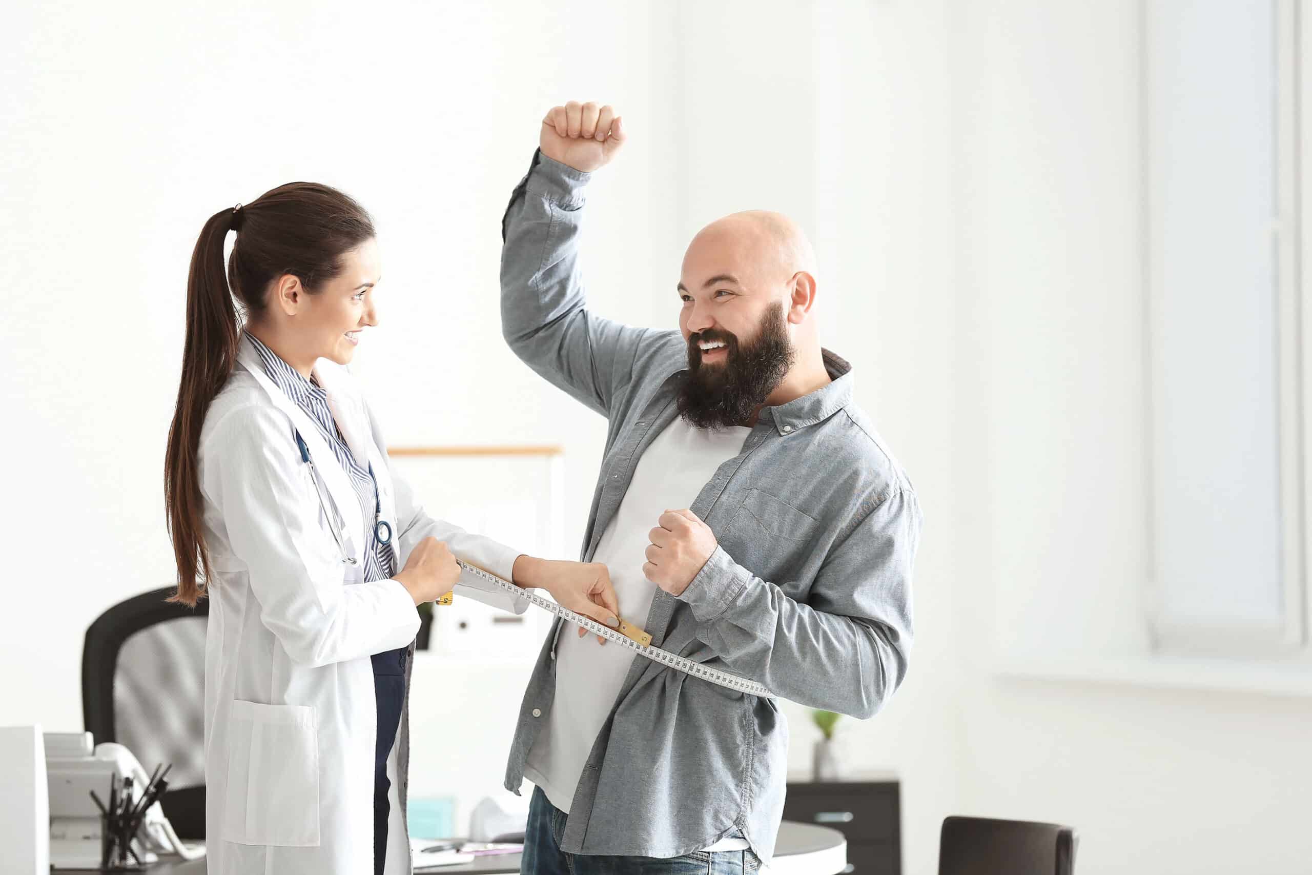 Young female doctor measuring waist of overweight man with centimeter in clinic